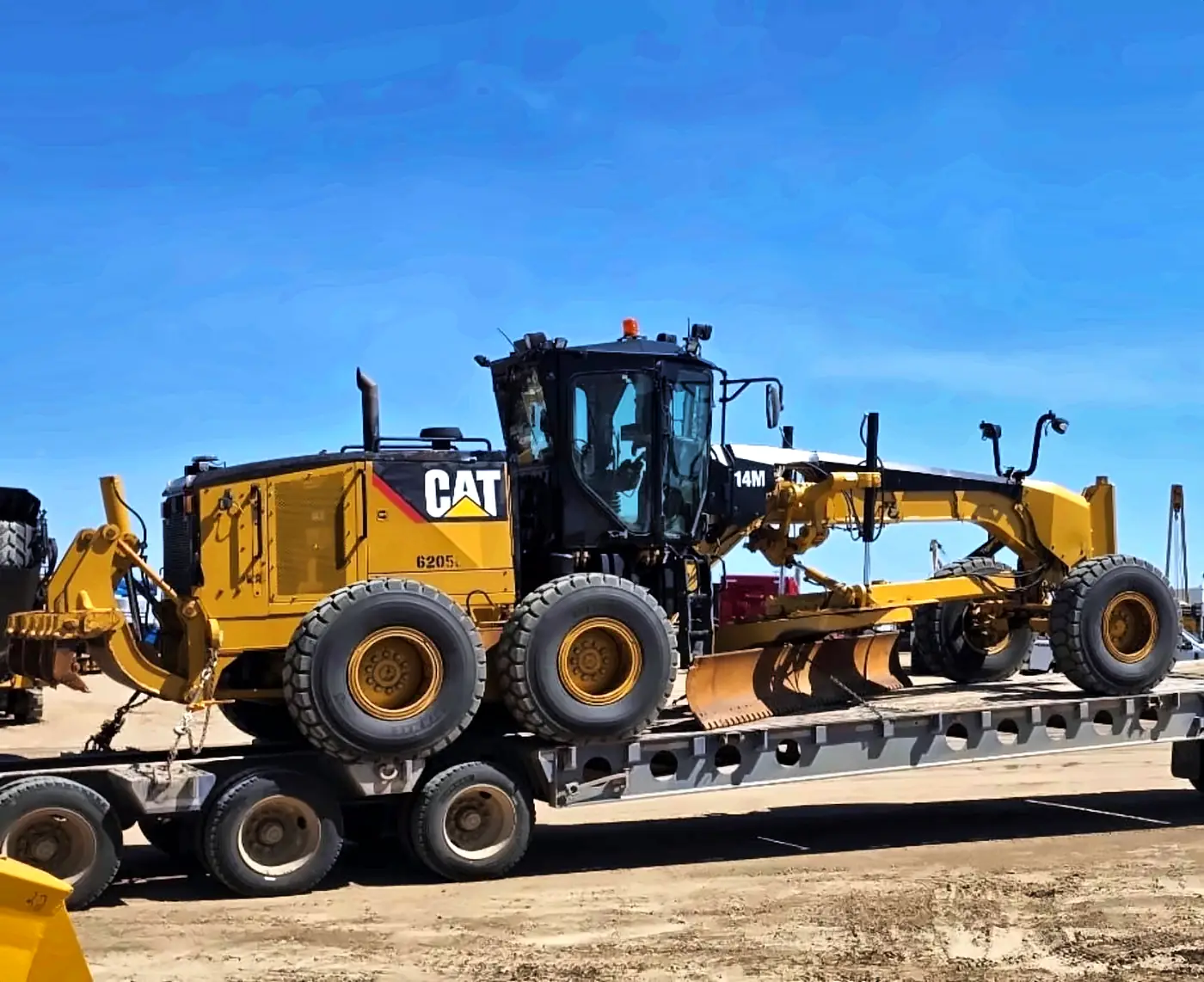 Ôsi Energy CAT 14M motor grader on a lowbed trailer